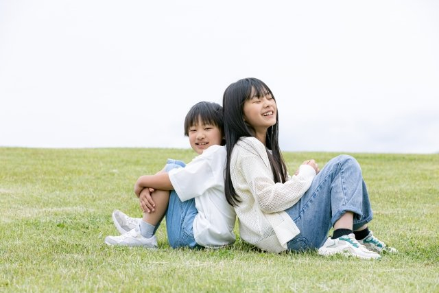 背中合わせで芝生の上に座っている男の子と女の子