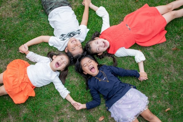 手を繋いで芝生に寝転がっている4人の子ども